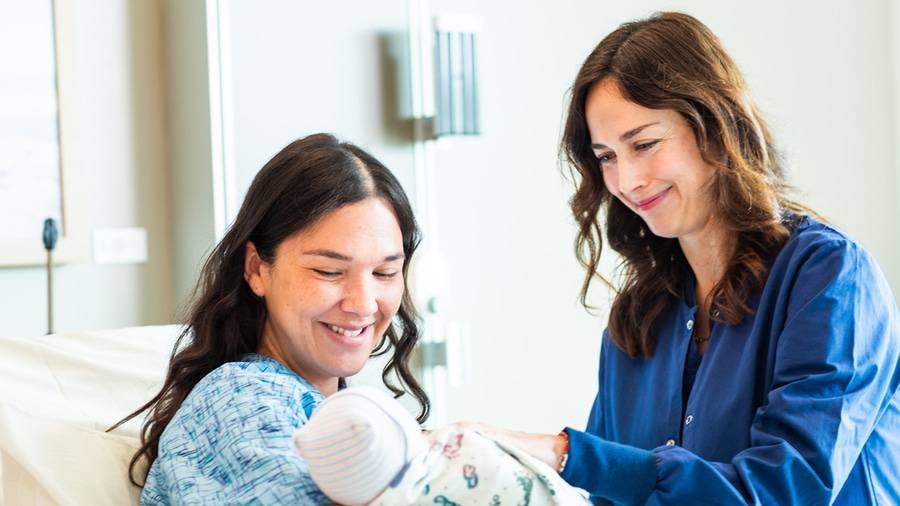 A new mother smiling at her healthy baby while speaking to a Scripps postpartum nurse.