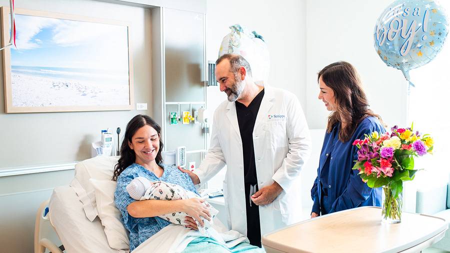 A mother smiling at her newborn baby as Scripps OB-GYN, Dr. Nikolas Capetanakis and a nurse check on her.