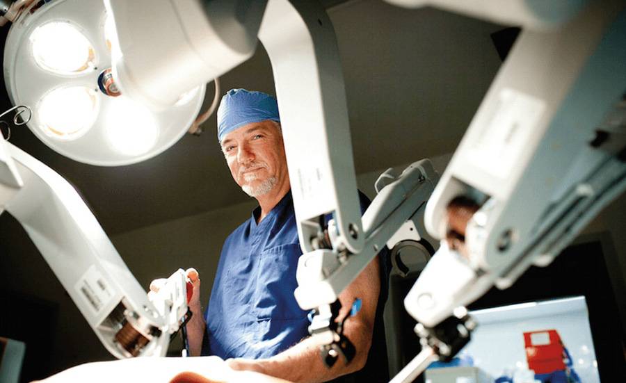 A surgeon stands next to a robot-assisted surgical device.