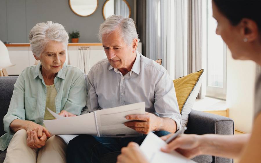 A man and woman with gray hair sit on the couch as they review charitable considers with a tax adviser.