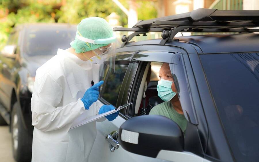 A Scripps Health employee reviews a coronavirus testing questionnaire with a patient from their vehicle.