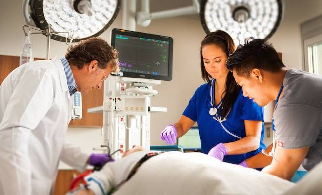 A physician and two nurses treat a patient in an emergency room.