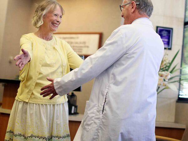 Mary Jennings-Smith smiles as she reaches to hug Michael Kosty, MD, who helped treat her cancer diagnosis.